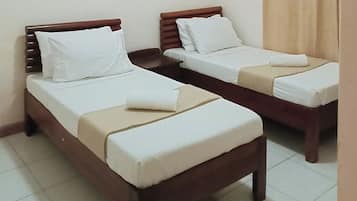 Two single beds with wooden headboards and white linens, arranged in a small room with tiled flooring.