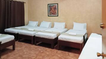 Habitación de hotel con cuatro camas individuales, una cortina marrón, un cuadro en la pared y una puerta con pomo de latón.