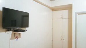 A room with a mounted television, a wardrobe, and a door. - Reddoorz @ Casa Marabella Villamonte Bacolod City (Bacolod)