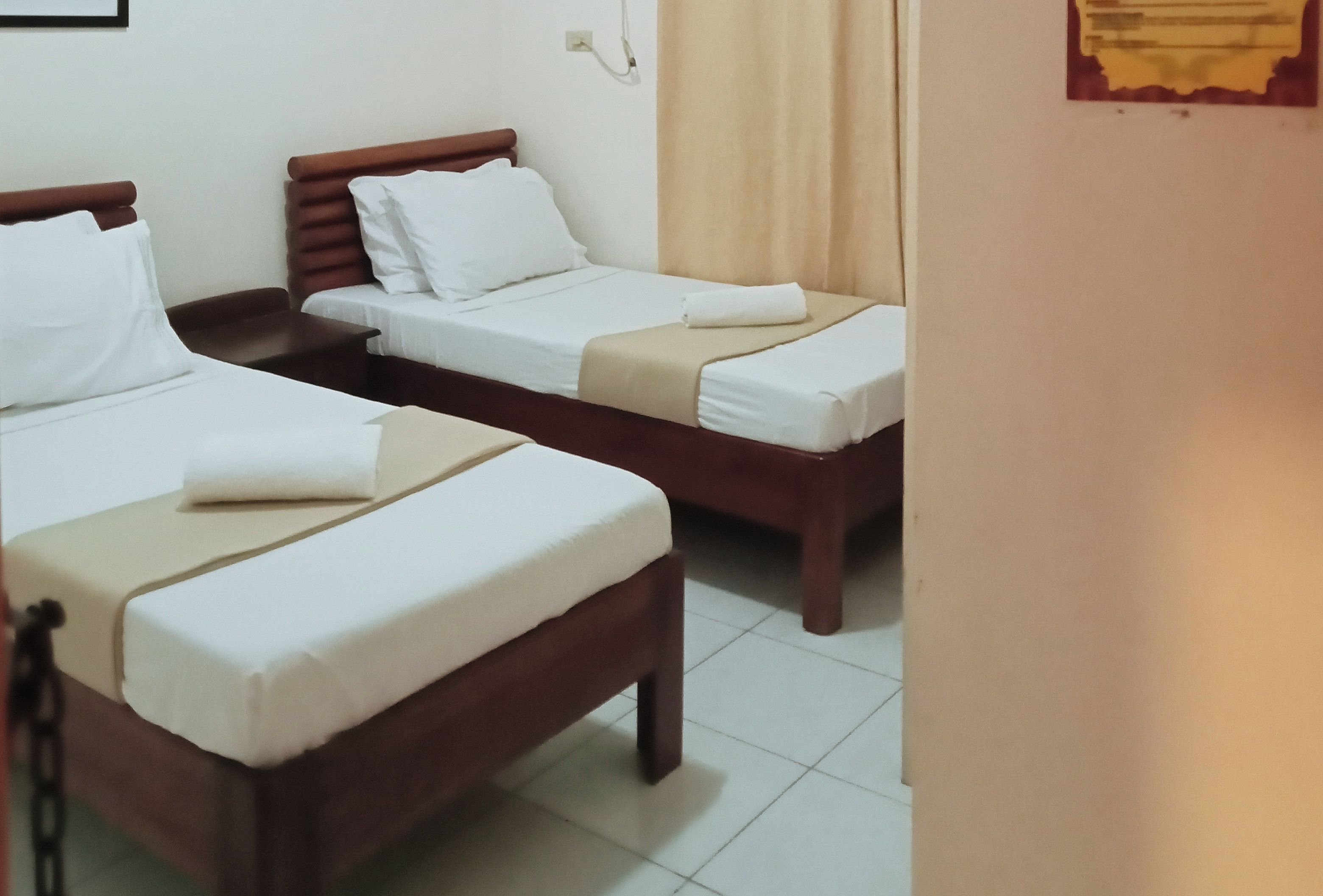 Een hotelkamer met twee eenpersoonsbedden, elk met een houten hoofdbord en wit beddengoed.