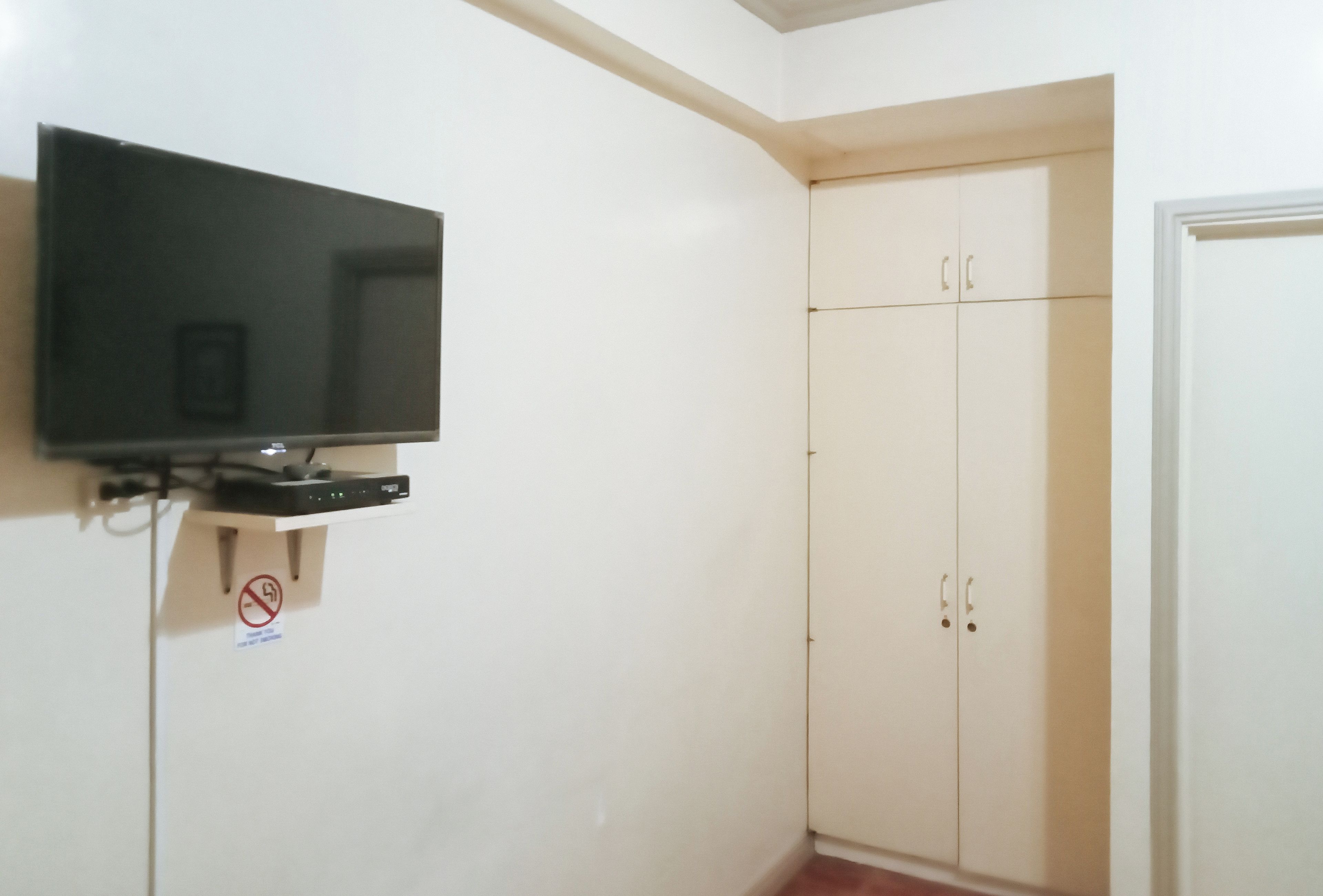 Een kamer met een televisie aan de muur, een kledingkast en een deur.