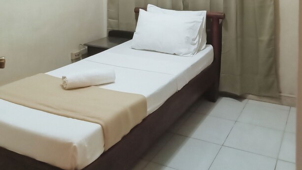 A single bed with a white mattress and a beige blanket, a wooden headboard, and a small bedside table with a lamp. - Reddoorz @ Casa Marabella Villamonte Bacolod City (Bacolod)