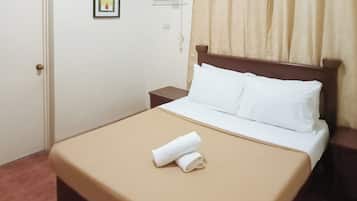 Una cama bien hecha con sábanas blancas y una colcha marrón, una mesita de noche pequeña y un equipo de aire acondicionado instalado en la pared.