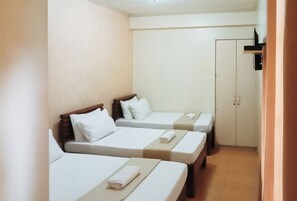 A hotel room with three single beds, each with a wooden headboard, white bedding, and a rolled towel. There is a wardrobe with two doors and a small shelf above it. - Reddoorz @ Casa Marabella Villamonte Bacolod City (Bacolod)