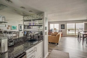 Una cocina con encimera de granito, horno empotrado y cafetera. Hay una zona de comedor con sofá y mesa.