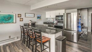 Una cocina moderna con una isla central, taburetes de bar, electrodomésticos de acero inoxidable y vistas al área de estar.