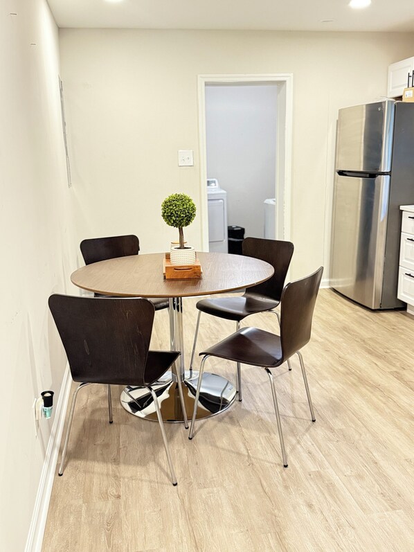 Una cocina moderna con una mesa redonda de comedor, cuatro sillas, una pequeña planta en maceta y un refrigerador de acero inoxidable.