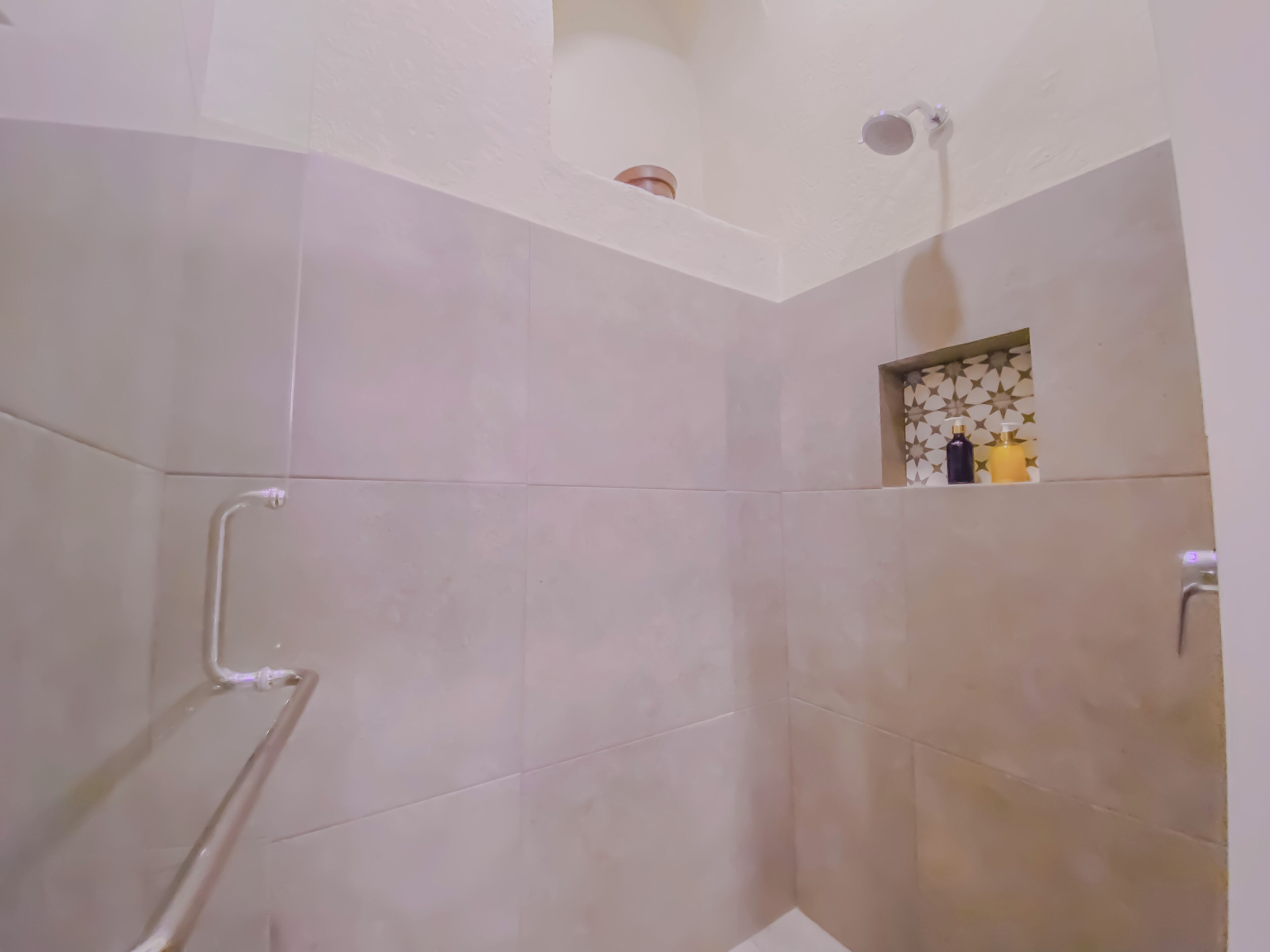 A shower area with beige tiles, a handrail, and a small shelf with toiletries.