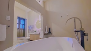 A modern bathroom with a large white bathtub, a round mirror, and a decorative wall with a circular pattern. - Cozy 1-bedroom suite in amazing Puebla with King size bed, WiFi and bathtub (Heroica Puebla de Zaragoza)