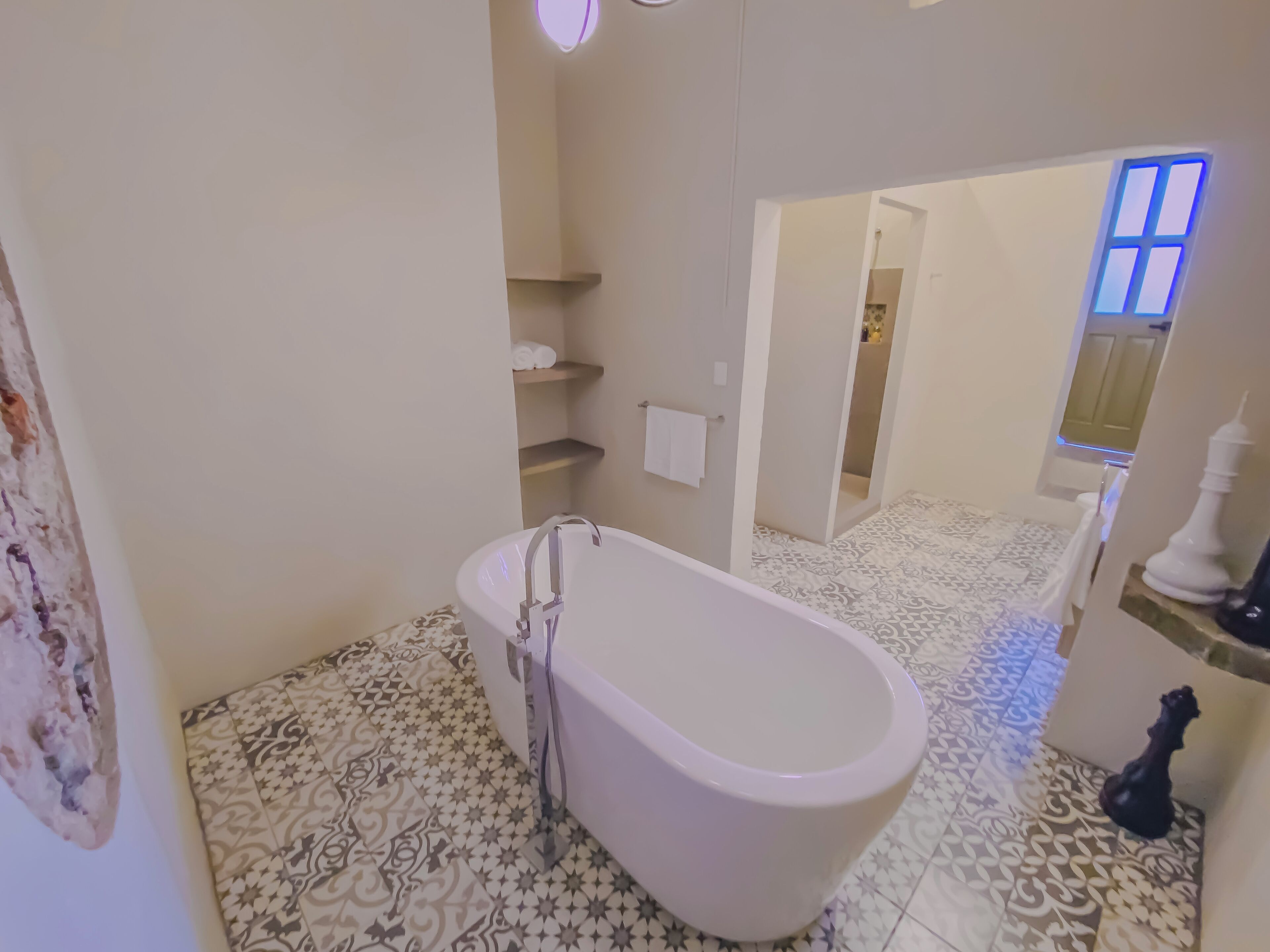 A bathroom with a freestanding bathtub, patterned floor tiles, a towel rack, and a mirror.