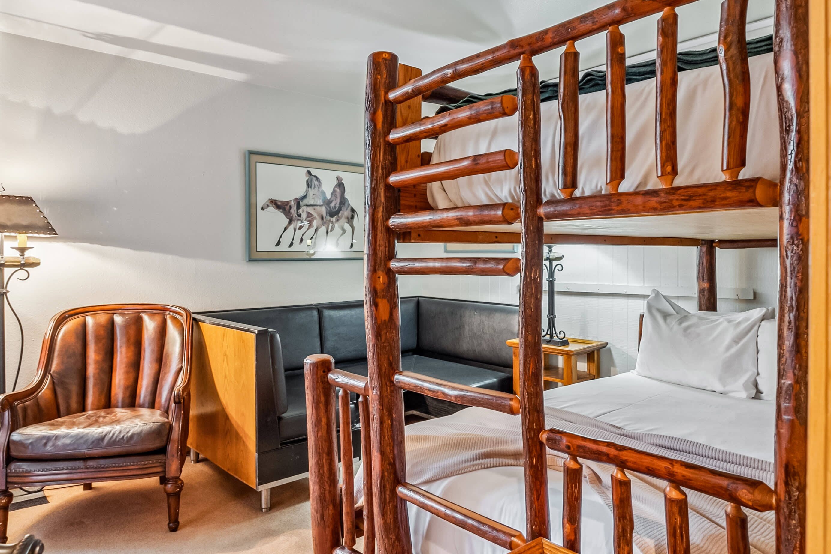 Una cama individual con estructura de madera, un sillón de cuero, un sofá y un cuadro enmarcado en la pared.