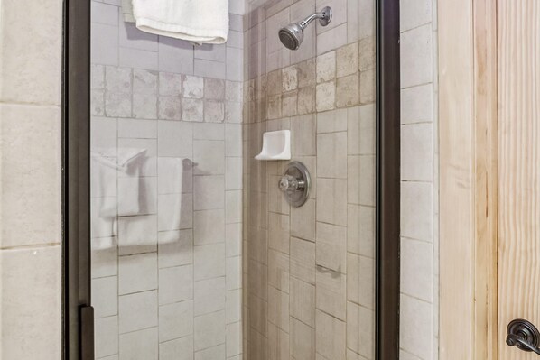 A shower with a glass door, tiled walls, and a wooden panel on the right.