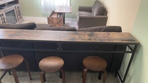 A kitchen with a wooden island, three stools, a sofa, and a cabinet. - The Purple Door -FRESHLY UPGRADED AIR CONDITIONING NOW AVAILABLE- (McGill)