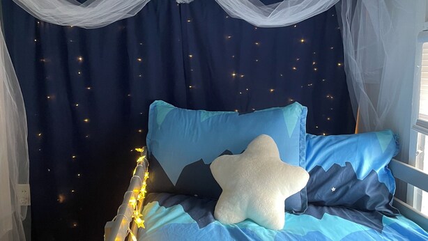 A bed with a star-shaped pillow and blue bedding, a canopy overhead, and fairy lights along the headboard. - The Purple Door -FRESHLY UPGRADED AIR CONDITIONING NOW AVAILABLE- (McGill)