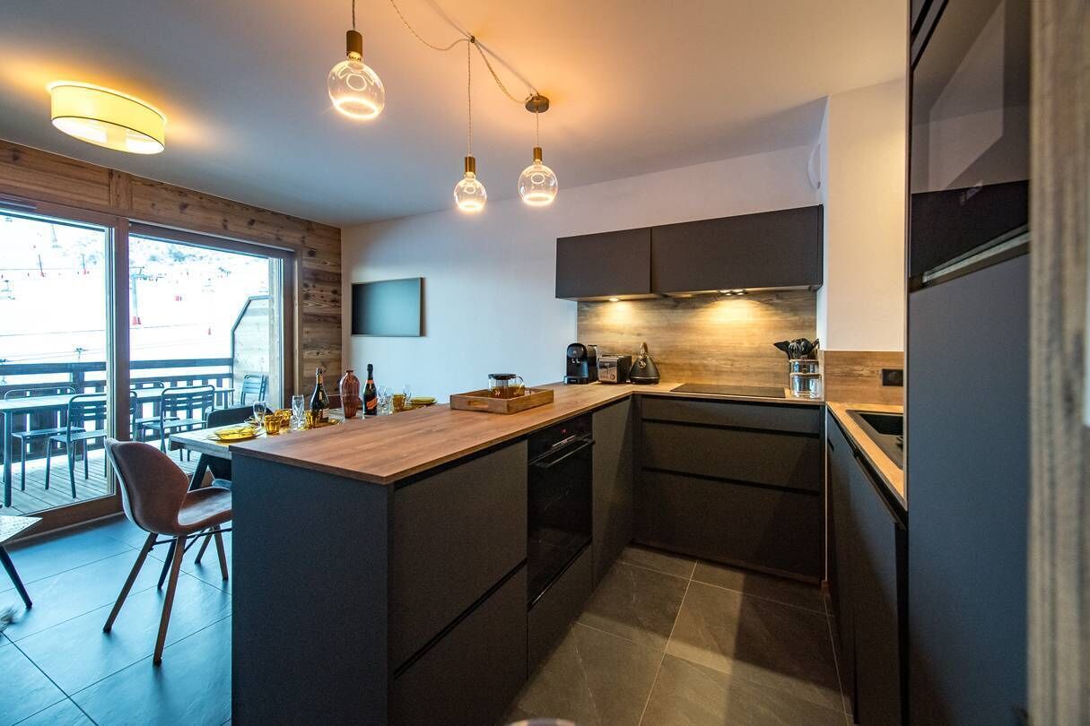 Een moderne keuken met een centraal eiland, donkere kastjes en hanglampen.