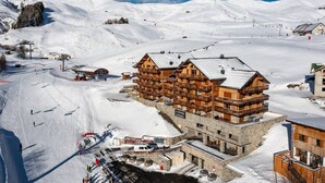 Eine Holzhütte mit mehreren Balkonen, gelegen an einem verschneiten Berghang mit Skipisten im Hintergrund.