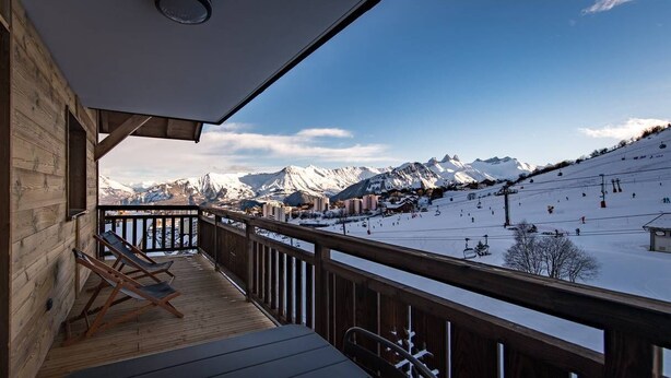 Eine Holzterrasse mit Blick auf eine verschneite Berglandschaft und Skipisten.
