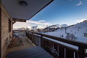 Une terrasse en bois offrant une vue sur un paysage montagneux enneigé et sur des pistes de ski.