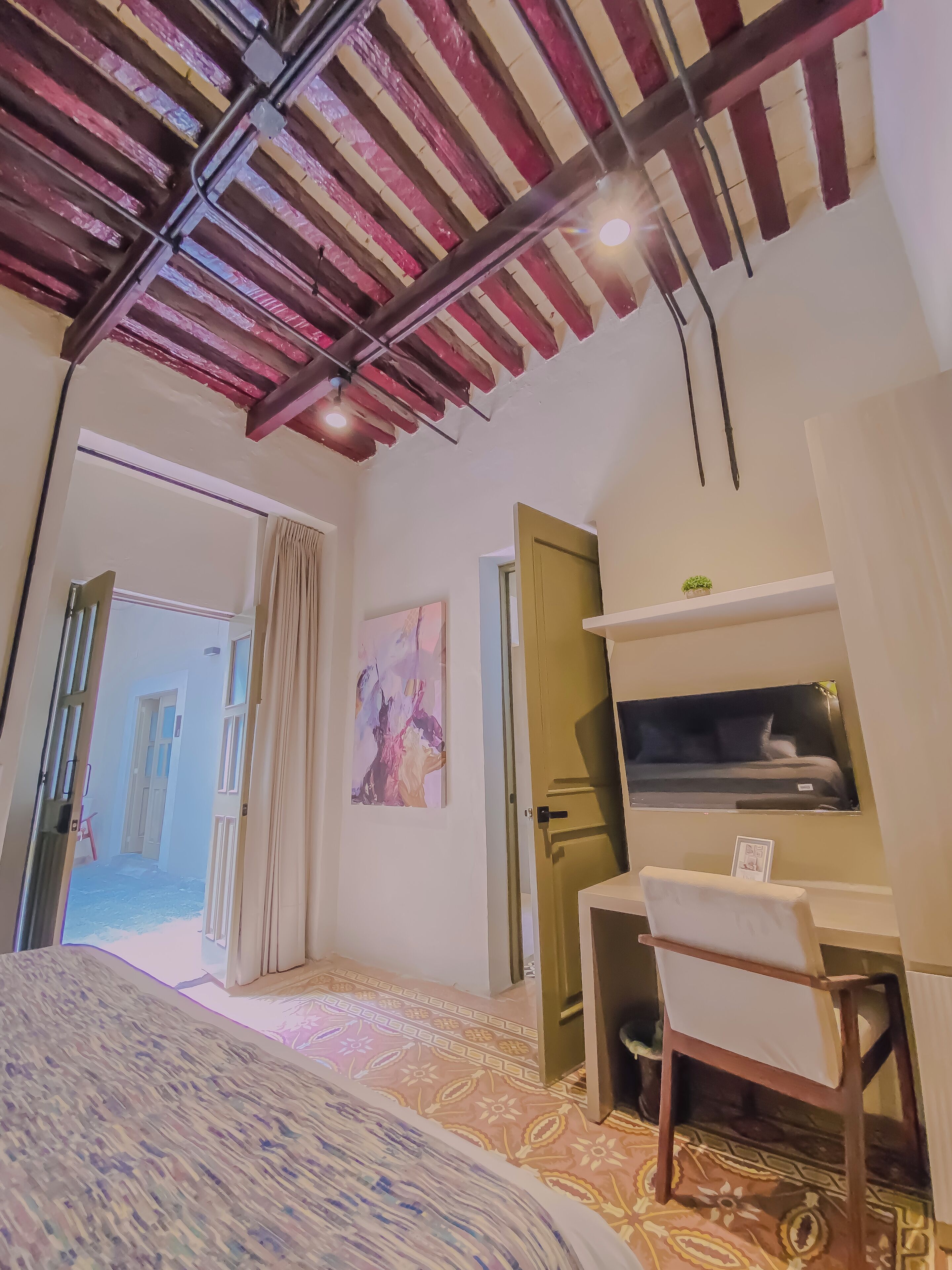 Un dormitorio con cama, un escritorio, una silla, un cuadro y una puerta que da a un balcón.