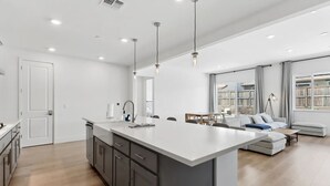Eine moderne Küche mit einer großen Kochinsel, ein Essbereich mit Tisch und Stühlen sowie ein Wohnzimmer mit Sofa und Couchtisch.