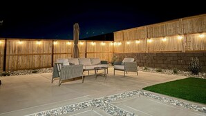 Ein Terrassenbereich im Freien mit Holzzaun, einer Couch, zwei Stühlen und einem kleinen Tisch.