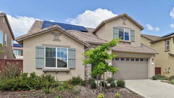 A residential house with a garage, a small tree in the front yard, and solar panels on the roof.