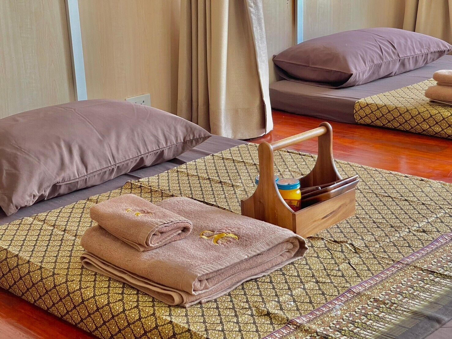 Una habitación ordenada con una cama, almohadas, una bandeja de madera con un tarro y toallas dobladas.