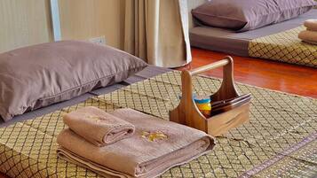 Una habitación ordenada con una cama, almohadas, una bandeja de madera con un tarro y toallas dobladas.