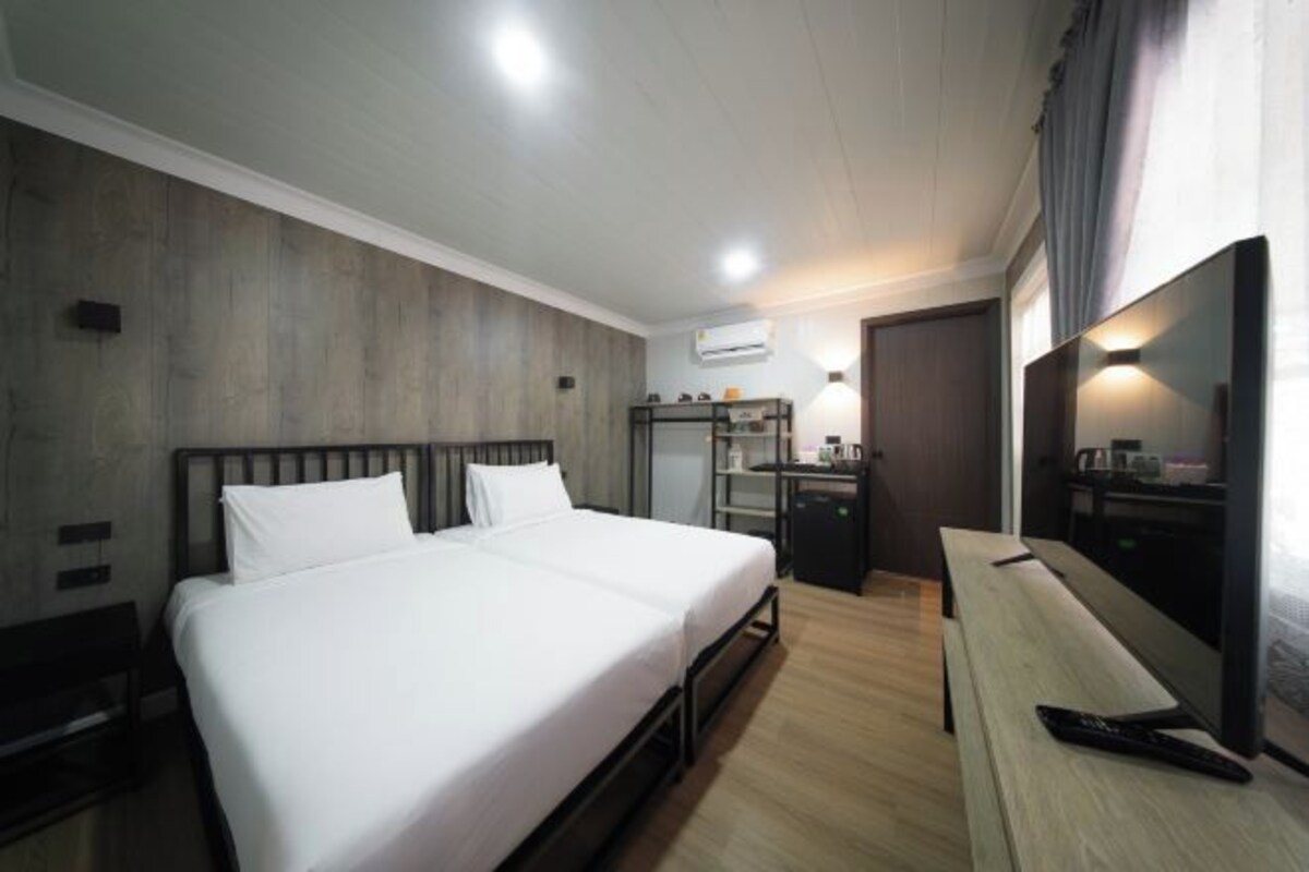 A hotel room with a bed, bedside tables, a desk, a chair, a TV, and an air conditioning unit.