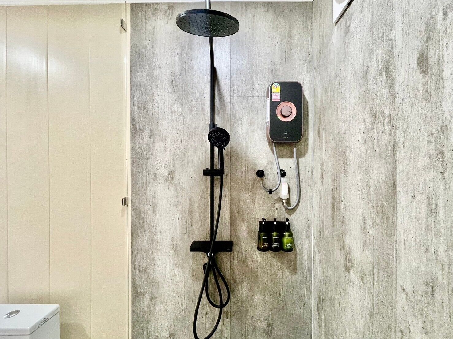 A shower with a handheld showerhead, a control panel, and a bottle of shampoo.
