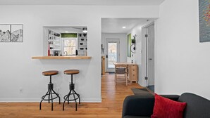 A modern living space with a kitchen area, wooden flooring, and a black sofa with a red cushion. - Overland Park Retreat (Overland Park)