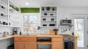 A modern kitchen with white cabinetry, a built-in stove, and a window with a view of trees. - Overland Park Retreat (Overland Park)