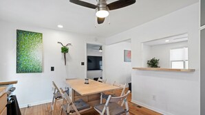 A modern dining area with a wooden table and chairs, a ceiling fan, and a green wall art piece. - Overland Park Retreat (Overland Park)