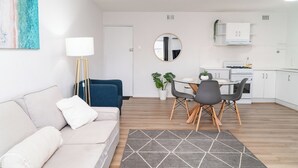 A modern living room with a sofa, a coffee table, and a dining area with chairs and a small table. - Spacious & Cosy Self-Contained 2 Bedroom Apartment (Rivervale)