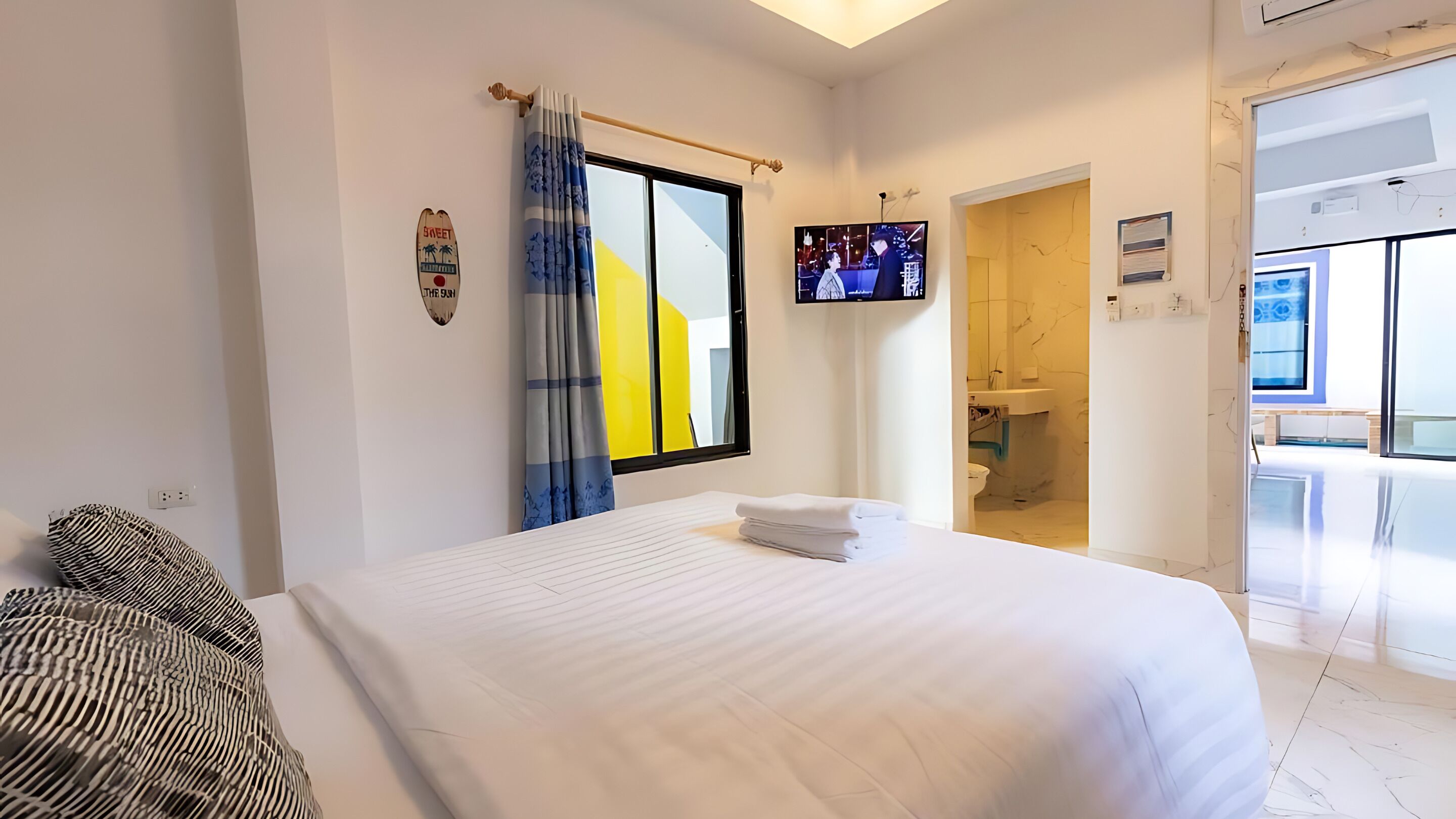 A hotel room with a bed, a television, a bathroom, and a view of the outside.