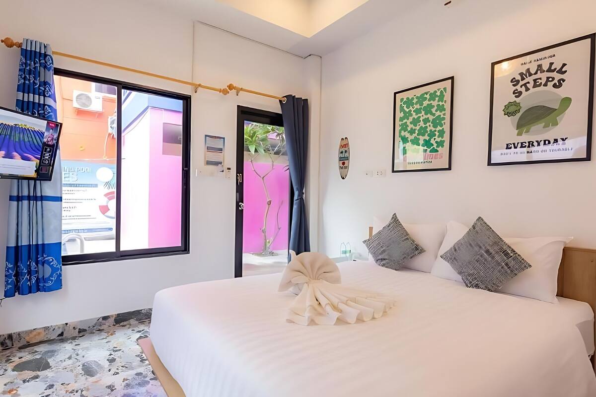 A hotel room with a bed, a TV, a window with curtains, and two wall art pieces.