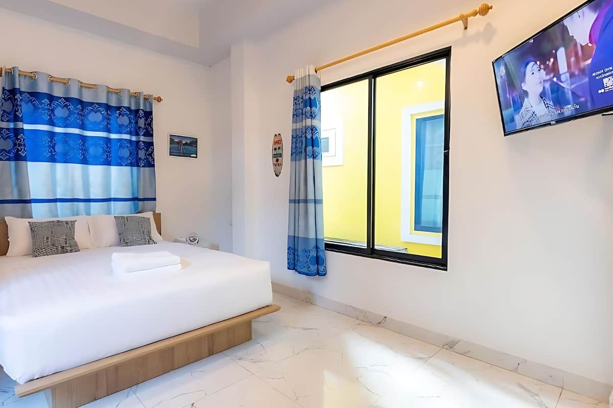 A hotel room with a bed, a wooden bench, a TV, and a window with curtains.