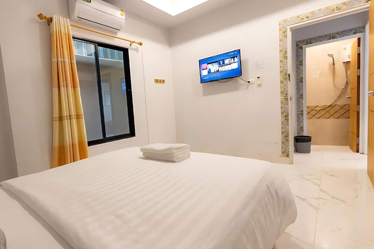 A hotel room with a bed, a TV mounted on the wall, and a window with curtains.