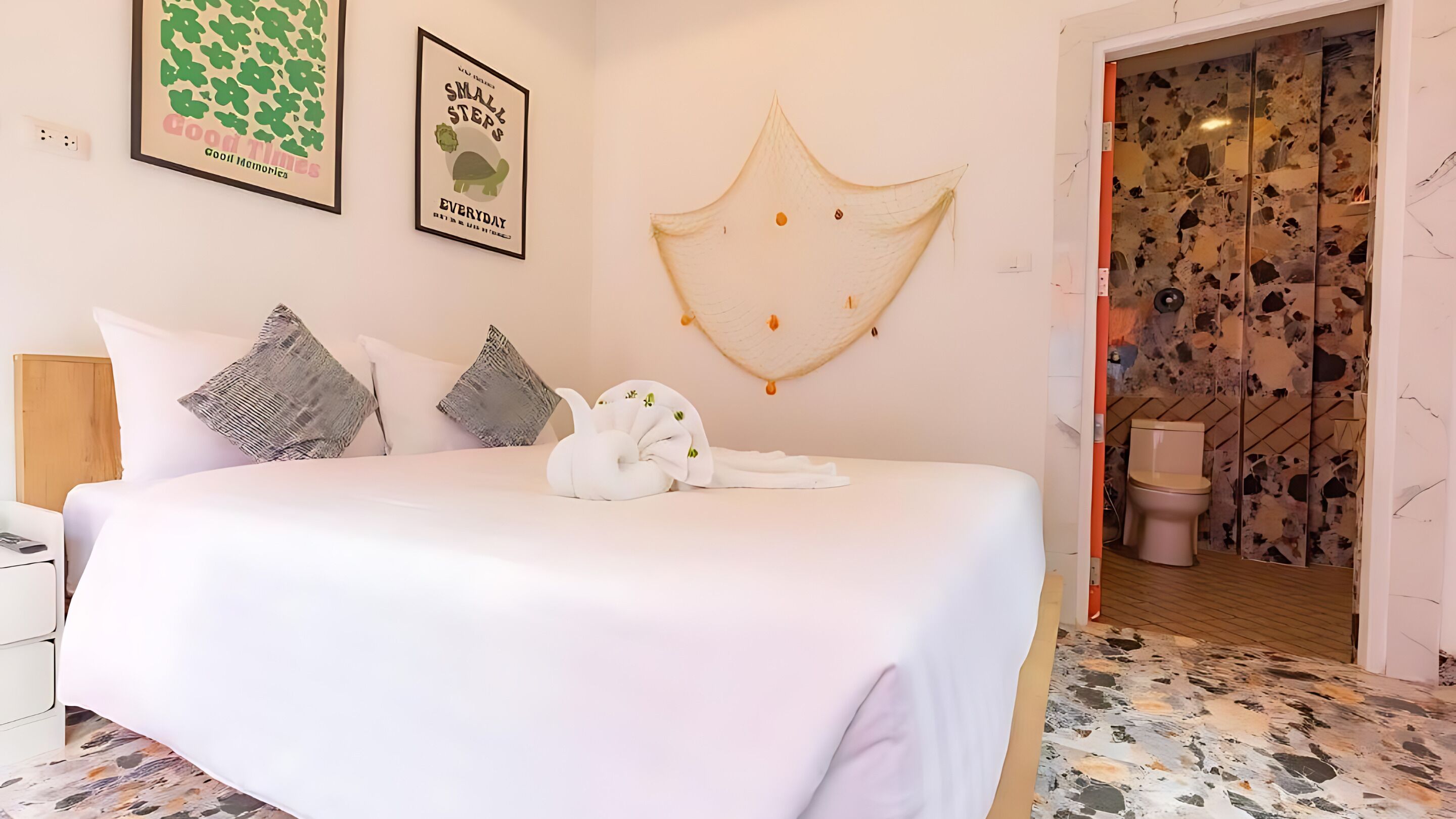 A neatly made bed with pillows, a wall art piece, and a bathroom visible through an open door.