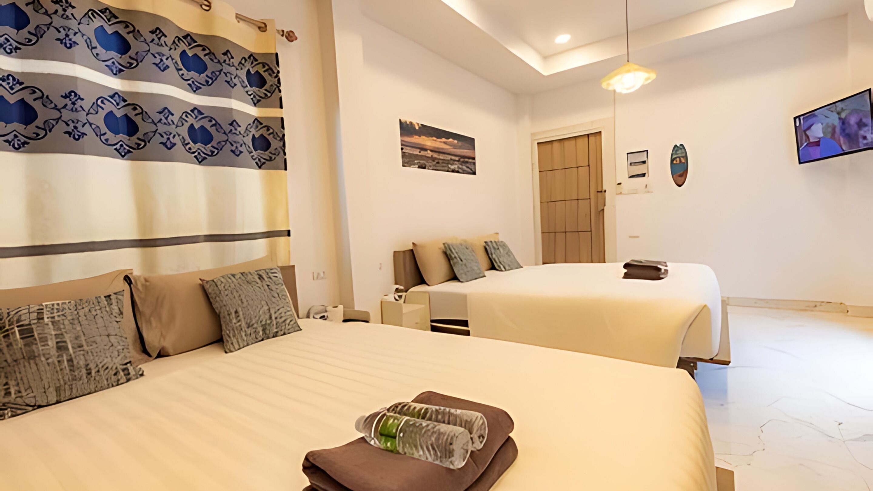 A hotel room with two beds, a large window, a painting on the wall, and a TV mounted on the wall.