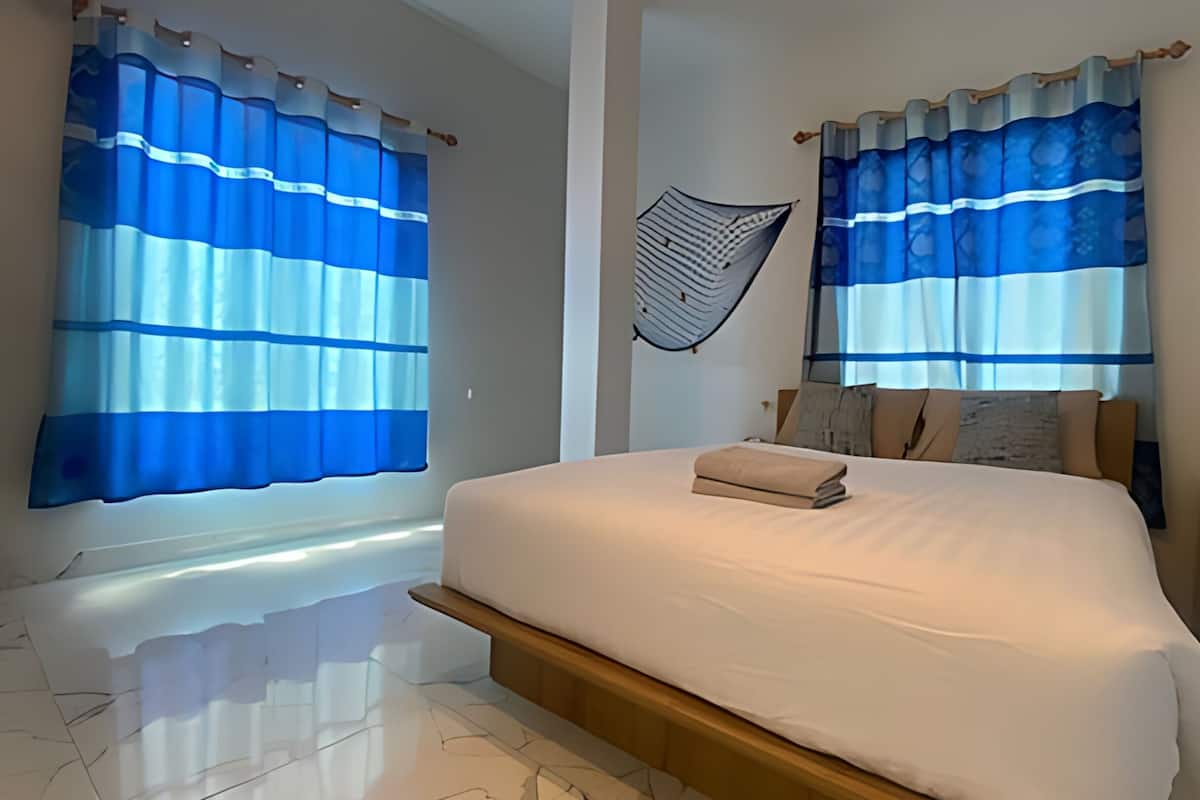A modern bedroom with a large bed, two windows with blue curtains, a wall-mounted hammock, and a small bedside table.