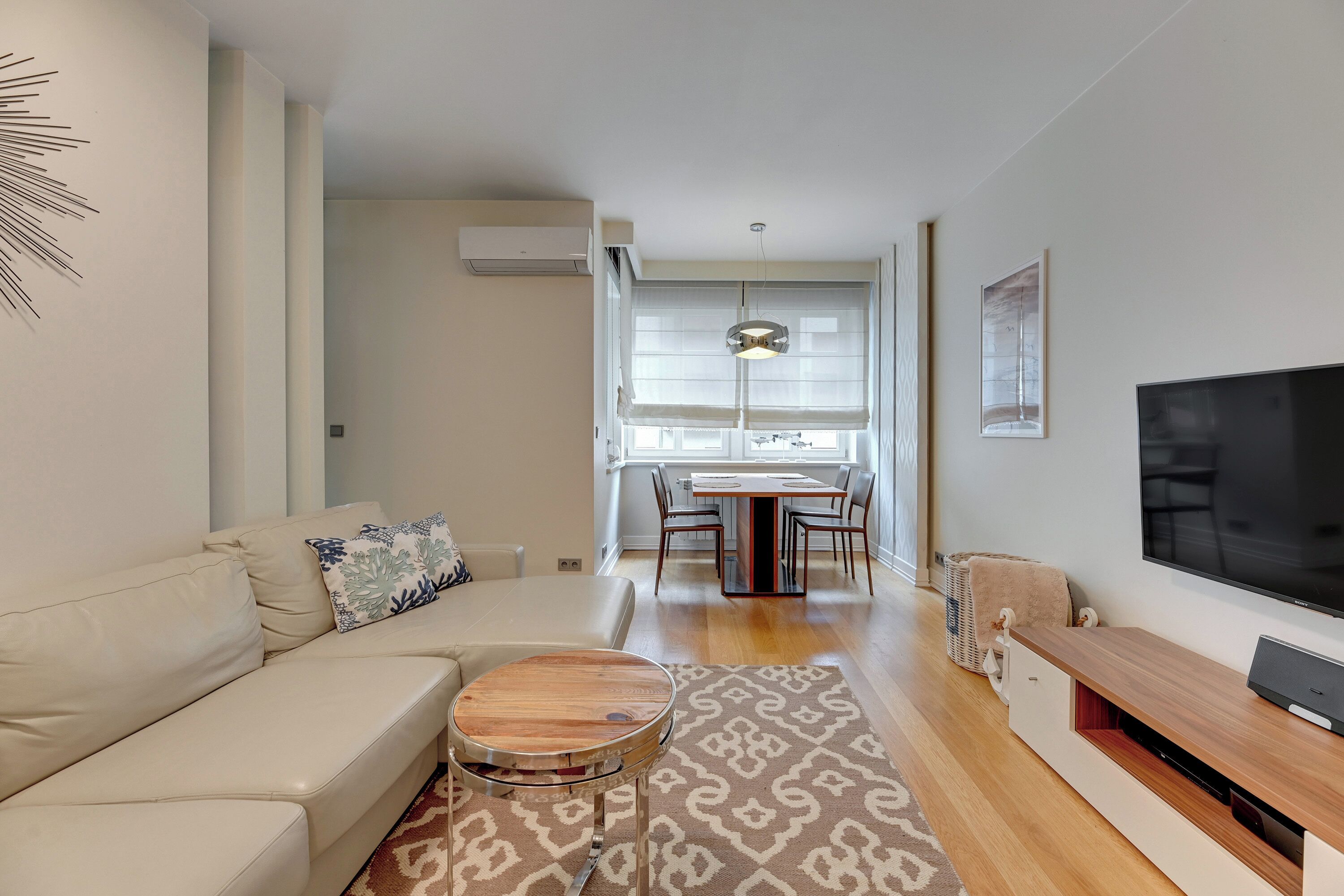 A modern living room with a sofa, coffee table, TV, and dining area.