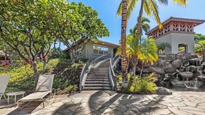 A stone staircase leading to a building with a tiled roof, surrounded by lush greenery and a small waterfall.