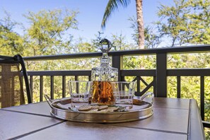 A table with a tray holding a decanter, glasses, and cookies on a balcony with a view of trees.
