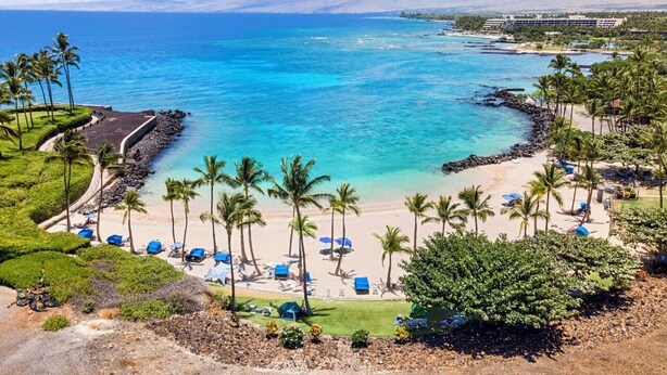 A beach resort with a clear view of the ocean, palm trees, and a hotel in the background.