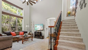 A spacious living room with a large window, a staircase, and a television.