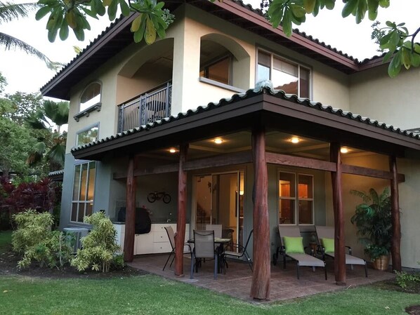 A two-story house with a covered patio area, a balcony, and a dining area with outdoor furniture.