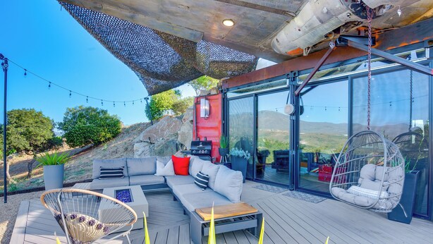 An outdoor deck with a sofa, a hanging chair, and a table. - Fallbrook Airplane Home w/ Fire Pit & Mtn Views! (Fallbrook)