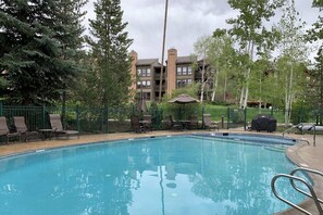 A swimming pool with lounge chairs and a barbecue grill, surrounded by a fence and trees.