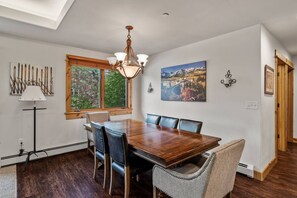 A dining room with a wooden table, leather chairs, a chandelier, and artwork on the walls.